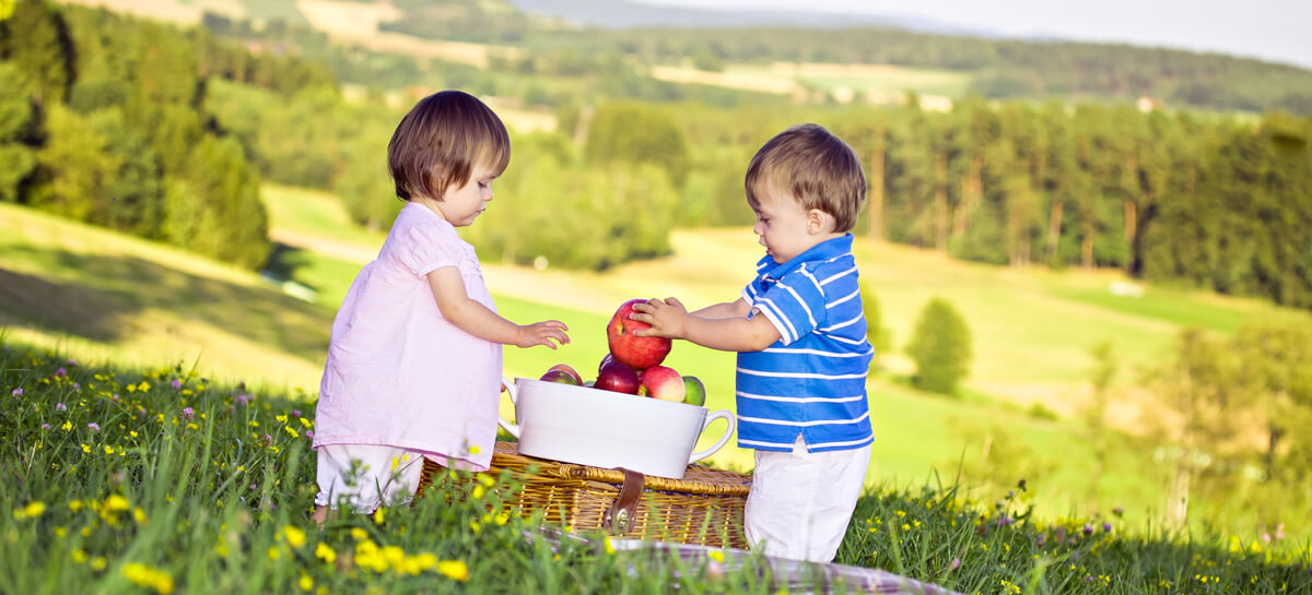 Zwei kleine Kinder reichen sich Äpfel