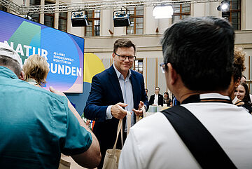 Bundesumweltminister Carsten Schneider verteilt Gewinne an die Besucherinnen und Besucher.. Weitere Informationen siehe Bildunterschrift