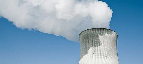 Kernkraftwerk mit dampfendem Turm vor dem klaren blauen Himmel.