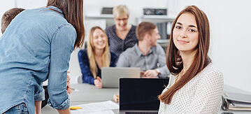 Junge Geschäftsfrau, die in einem modernen Großraumbüro arbeitet und in die Kamera lächeln.
