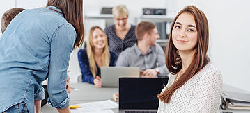 Junge Geschäftsfrau, die in einem modernen Großraumbüro arbeitet und in die Kamera lächeln.