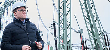 Bundesumweltminister Schneider mit Helm steht vor Strommasten