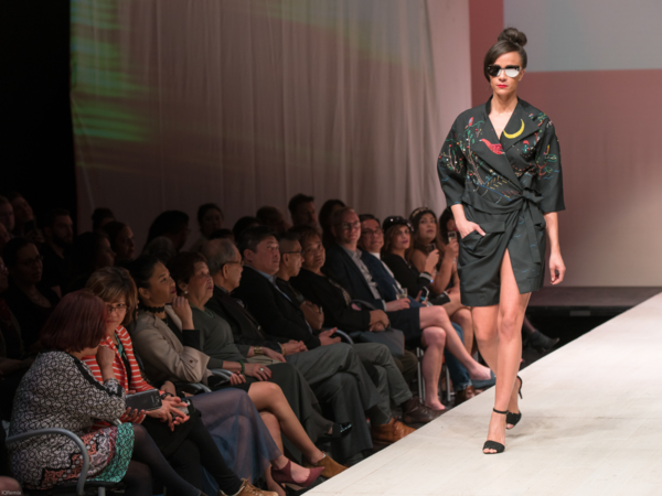 Frau mit schwarzem Oberteil läuft auf Laufsteg.