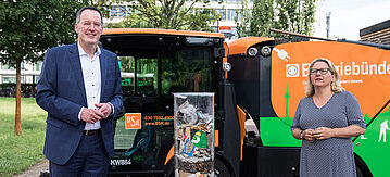 Bundesumweltministerin Svenja Schulze und Michael Ebling, VKU-Präsident und Oberbürgermeister von Mainz, stehen vor einer Kehrmaschine und einem Behälter mit Plastikmüll und Zigarettenkippen.