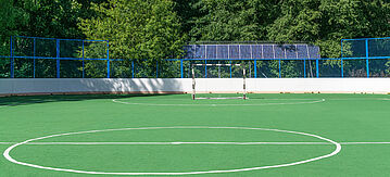 Sportplatz in der Nähe eines Waldes, Sonnenkollektoren sind hinter dem Zaun installiert.