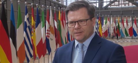 Carsten Schneider steht vor europäischen Flaggen in Brüssel und gibt ein Interview.