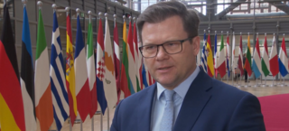 Carsten Schneider steht vor europäischen Flaggen in Brüssel und gibt ein Interview.