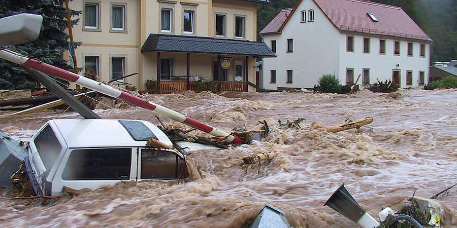 Ein Auto wird von braunem Wasser durch ein Dorf geschwemmt.