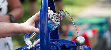 An einem Trinkwasserbrunnen wird eine Flasche mit Wasser gefüllt.. Weitere Informationen siehe Bildunterschrift