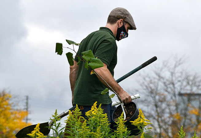 Ein Landschaftspfleger geht mit Schaufel und Eimer über eine Wiese.