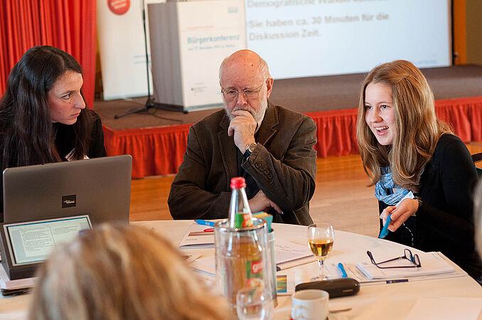 Älterer Herr hört zwei Schülerinnen interessiert zu 