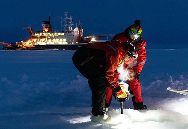 Zwei Umweltwissenschaftler*innen machen eine Bohrung im Eis. 