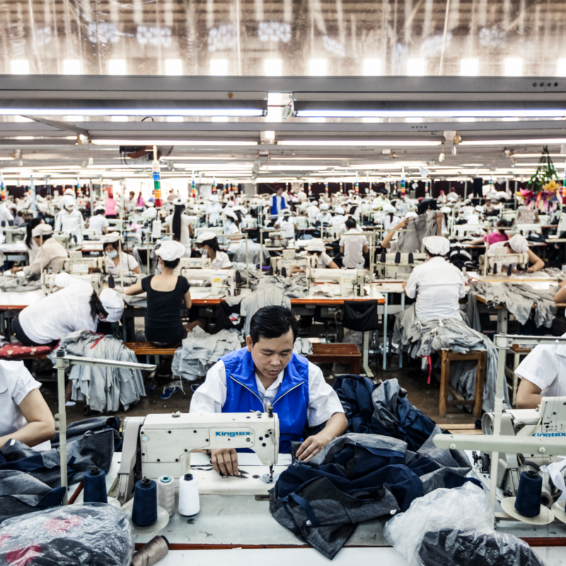 Große Fabrik mit Menschen an Nähmaschinen.