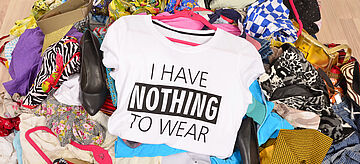 Ein Haufen mit Textilien und einem T-Shirt mit der Aufschrift "I have nothing to wear". Weitere Informationen siehe Bildunterschrift