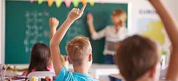Kinder heben ihre Finger im Unterricht, um sich für eine Antwort zu melden