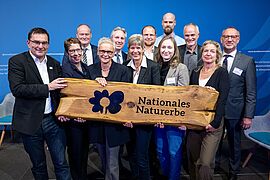 20 Jahre Nationales Naturerbe: Übergabe eines geschnitzten Holzbretts, das die Bedeutung und Verantwortung für das Naturerbe symbolisiert