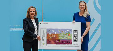 Zwei Personen halten eine riesige Briefmarke