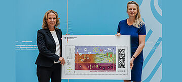 Zwei Personen halten eine riesige Briefmarke