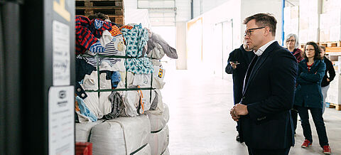 Carsten Schneider steht vor einem vollen Regal Altkleidung.