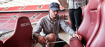 Ein Mann misst einen Sitz im Stadion aus.