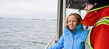 Steffi Lemke und ein Mann blicken auf einem Schiff in die Ferne.