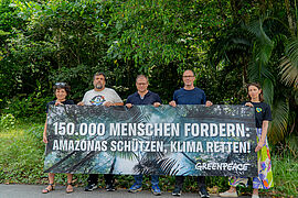 Vier Personen und Carsten Schneider halten ein Greenpeace-Transparent: 150.000 Menschen fordern: Amazonas schützen, Klima retten!