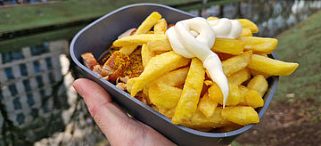 Bild: eine Hand hält eine Mehrwegschale mit Pommes mit Mayo und Currywurst