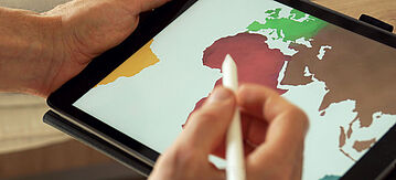 Mit Kreide auf einen Tisch gemalte Weltkugel. Um den Tisch sitzen Menschen