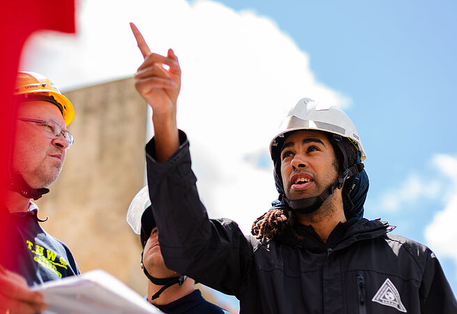 Eine Person mit Sicherheitshelm zeigt auf etwas.