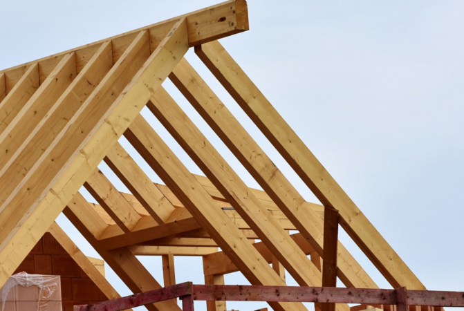 Ein Dachstuhl aus Holz vor einem blauen Himmel.