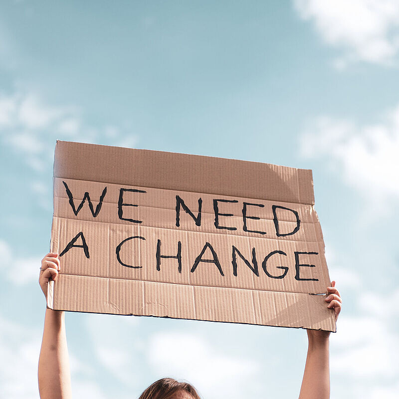 Eine Person hält ein Schild aus Pappe hoch.
