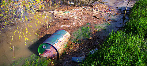 Fässer mit Giftmüll werden zusammen mit Plastikflaschen und anderem Müll in den Fluss gekippt und verschmutzen das Ökosystem.