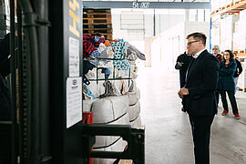 Carsten Schneider steht vor einem Regal voller Altkleidung.