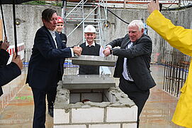 Jochen Flasbarth und eine weitere Person heben den Grundstein.