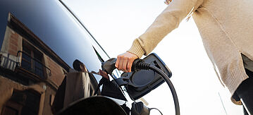 Eine Person steckt das Ladekabel ans E-Auto.