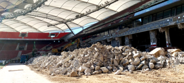 Ein großer Haufen Bauschutt in einem Stadion, im Hintergrund ist ein Bagger zu sehen.