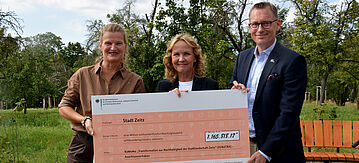 Drei Personen halten großen Scheck in die Kamera