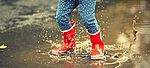 Kind springt mit seinen roten Gummistiefeln in einer Pfütze