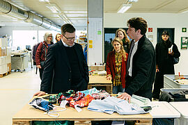 Carsten Schneider mit Mitarbeitenden der Deutschen Kleiderstiftung steht vor einem Tisch mit Altkleidern.