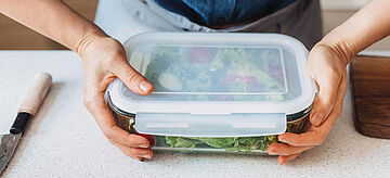 Hände einer Frau, die einen Salat in einen Glasbehälter verpackt