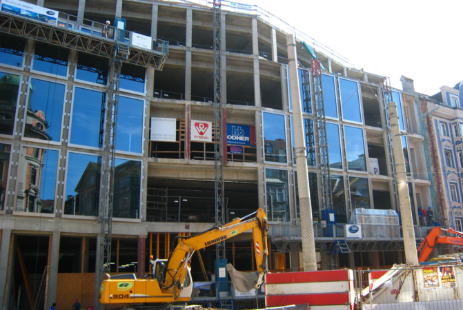 Eine Glasfront eines Gebäudes, vor dem ein Bagger steht und wo gebaut wird.