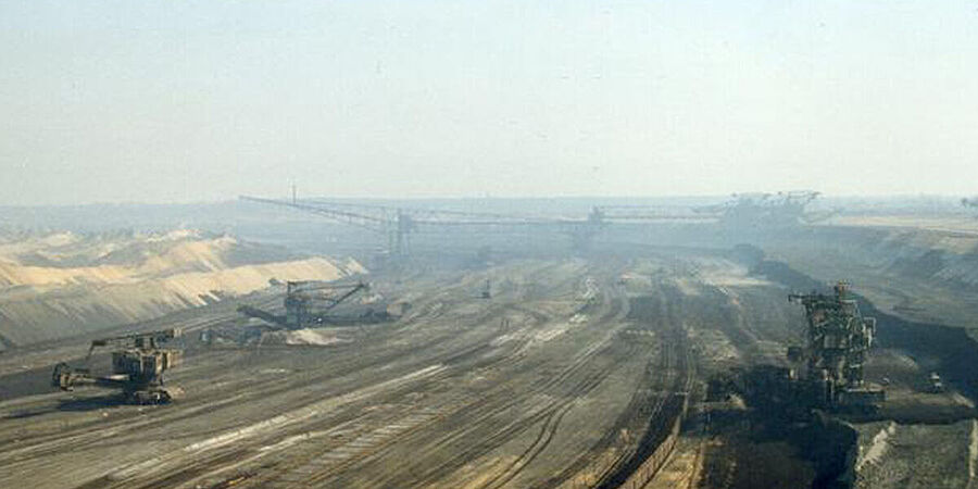 Blick vom Rand aus in die Grube eines riesigen Tagebaus. In der Grube mehrere Bagger 