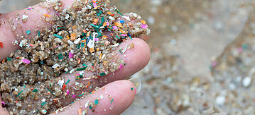 Nahaufnahme der Hände zeigt Mikroplastikabfälle, die mit dem Küstensand kontaminiert sind.