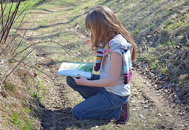 Eine Umweltpädagogin kniet auf einem Feldweg und macht sich Notizen.