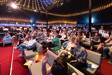 Publikum, welches auf die Bühne schaut und sich an der Diskussion beteiligt