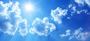 blauer Himmel mit Wolken und scheinender Sonne