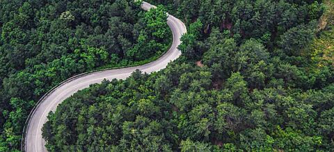 Luftaufnahme einer Bergstraße, die durch eine Waldlandschaft führt.