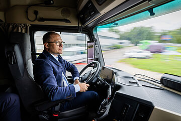 Carsten Schneider in einem Daimler Truck am Steuer. . Weitere Informationen siehe Bildunterschrift