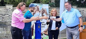 Steffi Lemke trinkt mit Vertreter der Stadt Querfurt ein Glas Wasser aus dem Trinkbrunnen