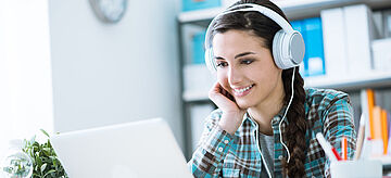 Junges Mädchen mit Kopfhörern sitzt am Laptop